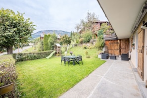 En terrasse med et bord og stole, et træhegn og udsigt til et bjerg.