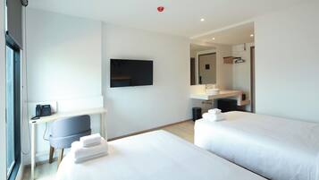 A modern hotel room with two beds, a desk, a chair, a flat-screen TV, a mirror, and a bathroom with a sink and towel rack.