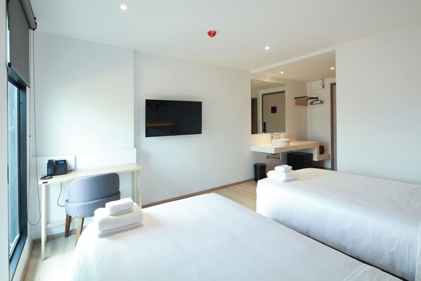 A modern hotel room with two beds, a desk, a chair, a flat-screen TV, a mirror, and a bathroom with a sink and towel rack. - KOO Hotel (Pak Kret)