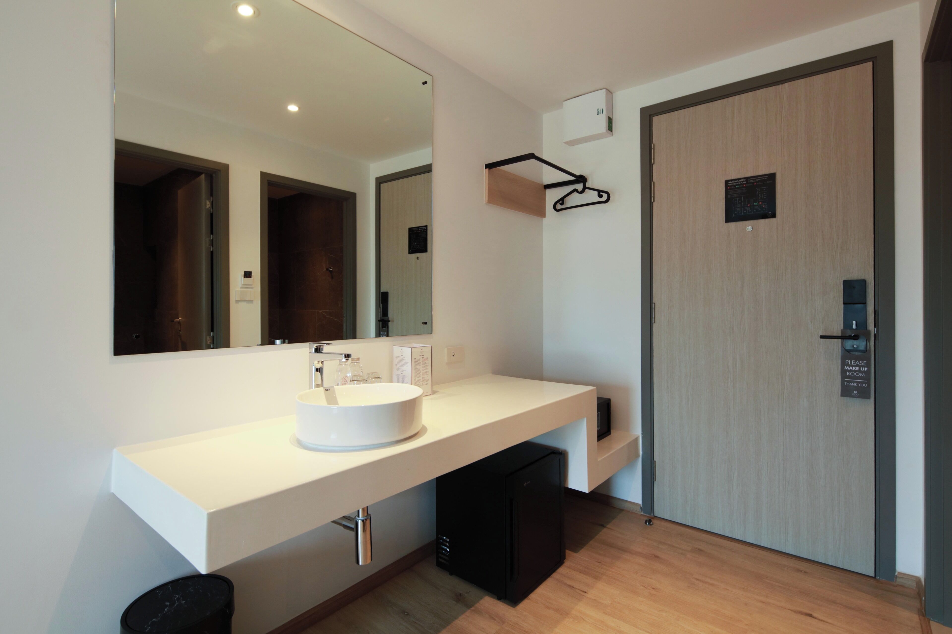 A modern bathroom with a white sink, a large mirror, and a wooden door.