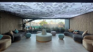 A modern lounge area with a geometric patterned ceiling, comfortable seating, and a large window offering a city view. - KOO Hotel (Pak Kret)