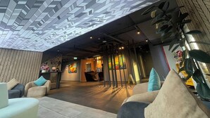 A modern lobby with a geometric patterned ceiling, comfortable seating, and a reception area with artwork. - KOO Hotel (Pak Kret)