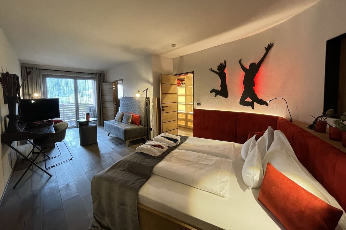 A modern hotel room with a large bed, a desk, a TV, and a balcony.