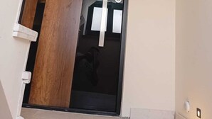 A modern door with a wooden panel and a glass panel, white wall trim, and a light switch on the wall.