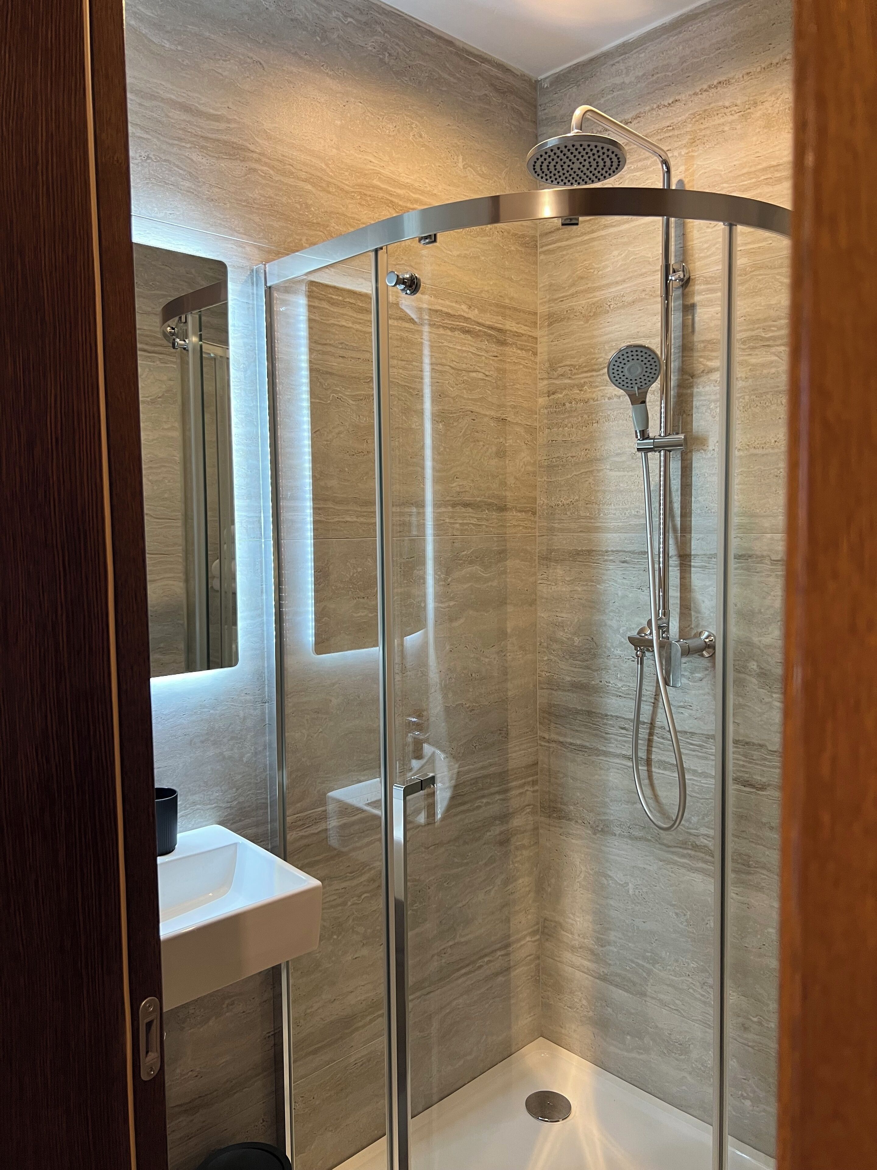 Een moderne douchecabine met een glazen deur, een handdouche en een douchekop aan de muur.