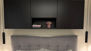 A modern bedroom with a large bed, grey headboard, and a black cabinet above the bed.