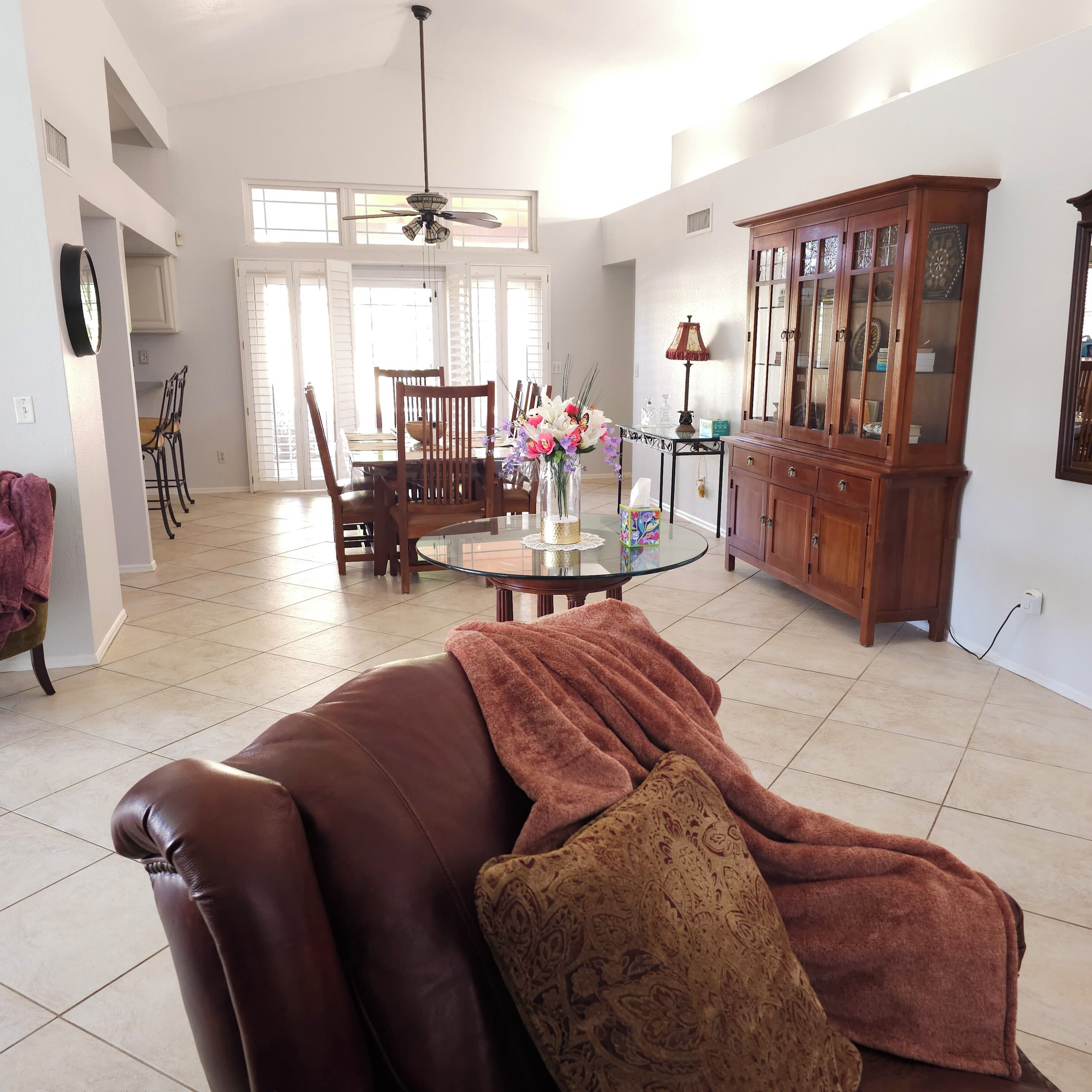A spacious living room with a leather sofa, a dining area with a glass table, and a wooden cabinet.