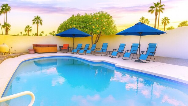 A swimming pool with blue chairs and umbrellas, surrounded by palm trees and a sunset sky. - Scottsdale Adobe Retreat with Private Pool & Hot Tub, King beds, Fast 5G Wifi. (Scottsdale)