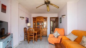 Una sala de estar con televisor, muebles de madera, ventilador de techo y un sofá naranja.
