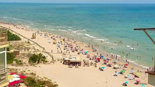 Una playa con un edificio a la izquierda y un muelle que se adentra en el agua.