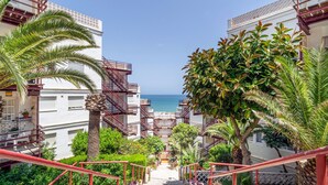 Una escalera conduce a un balcón con vistas a la costa, rodeado de vegetación exuberante y edificios blancos con barandillas rojas.
