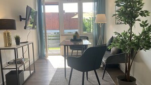 Un salon moderne avec un canapé, une table à manger et des chaises. On y trouve également une plante en pot, une lampe et un téléviseur posé sur un meuble.