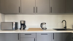 Une cuisine moderne avec des meubles gris, un four à micro-ondes, une machine à café et une bouilloire posés sur le plan de travail.