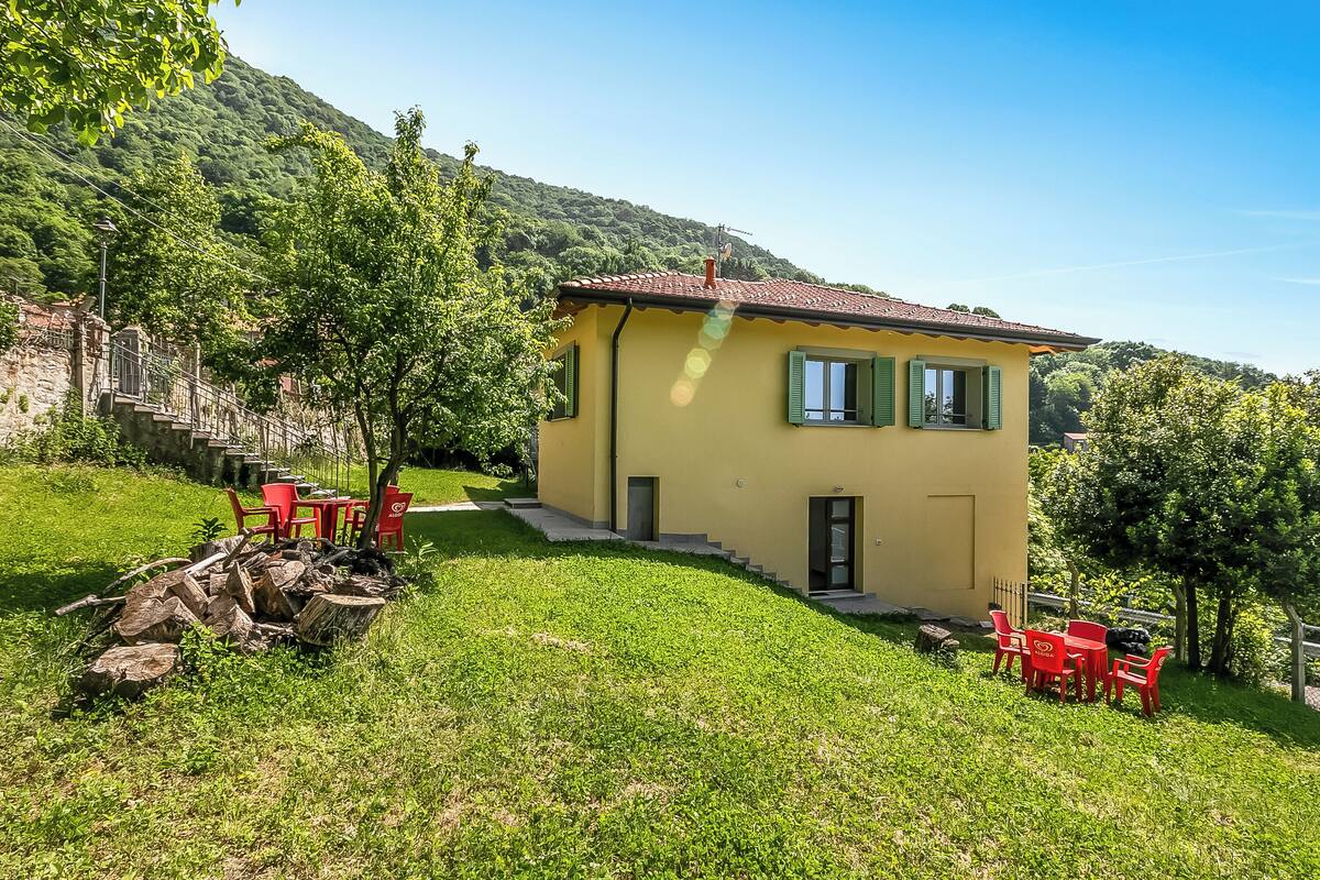 Una casa amarilla con techo rojo, contraventanas verdes y un pequeño porche con sillas y una mesa rojos.