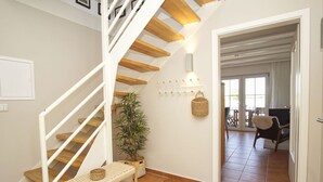 Una escalera con escalones de madera y barandas blancas que lleva a una habitación con un banco, una planta en maceta y un perchero de pared.