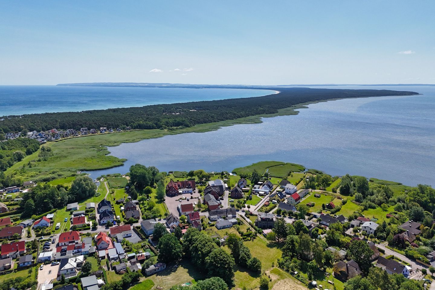 Vue aérienne d’un village côtier avec des maisons, un lac et une côte lointaine.