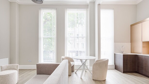 Una sala moderna con un sofá, dos sillones, una mesa redonda y una zona de cocina con armarios.