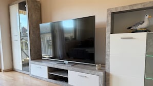 A modern living room with a flat-screen TV on a built-in stand, a white cabinet with glass doors, and a wooden floor.