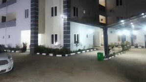 A multi-story building with a covered outdoor area, a car parked in front, and a green trash bin. - Bott Apartment (Abuja)