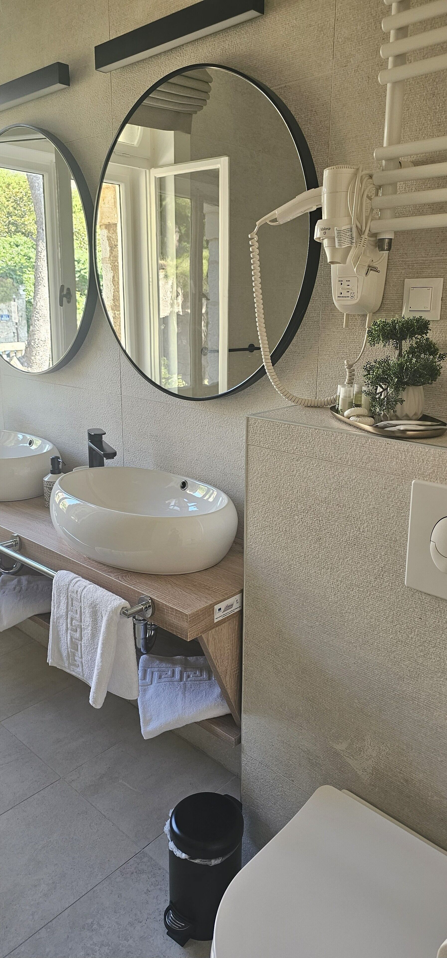 A bathroom with a round mirror, a sink, a hairdryer, and a small potted plant.