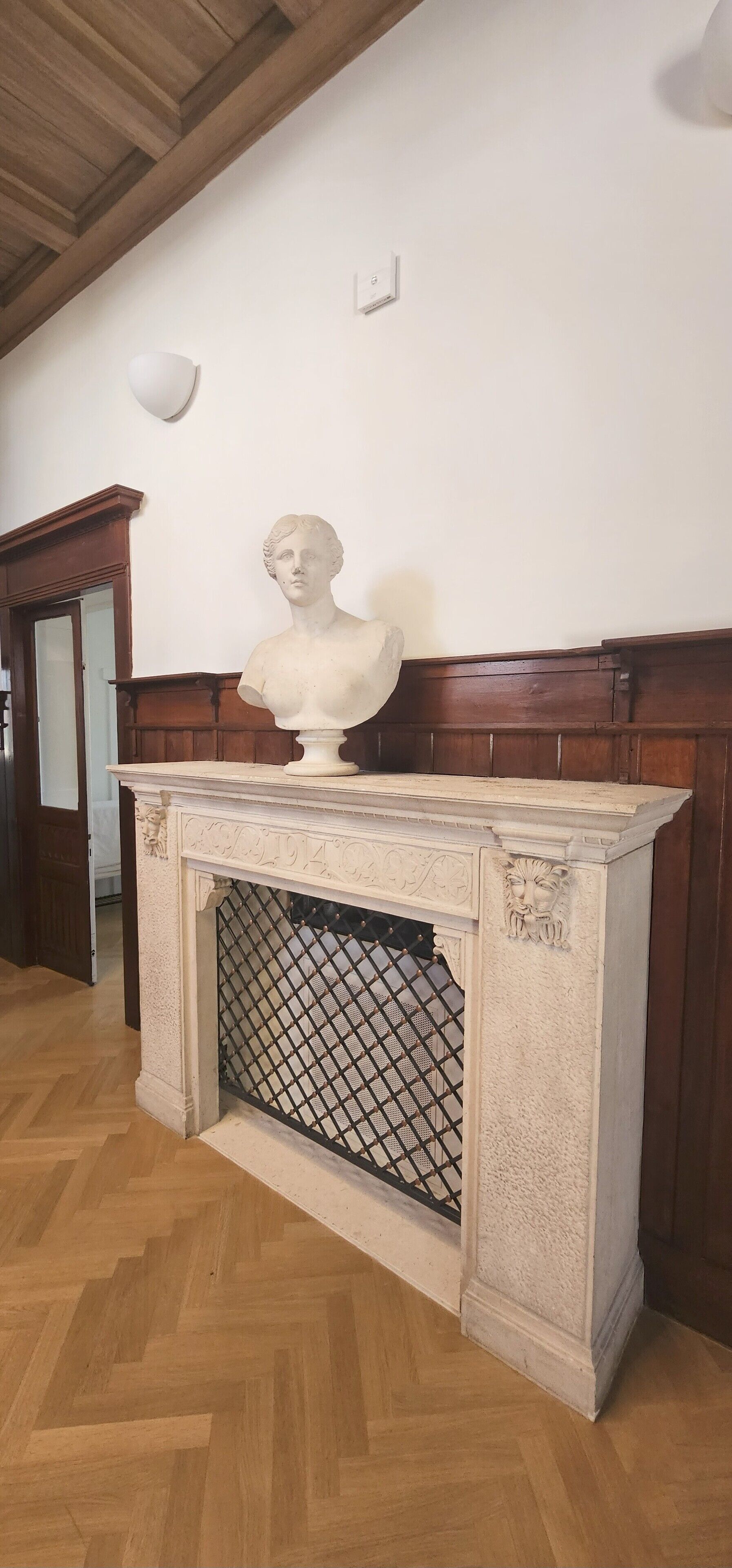 A marble fireplace with a bust sculpture on top, a wooden mantel, and a herringbone-patterned floor.