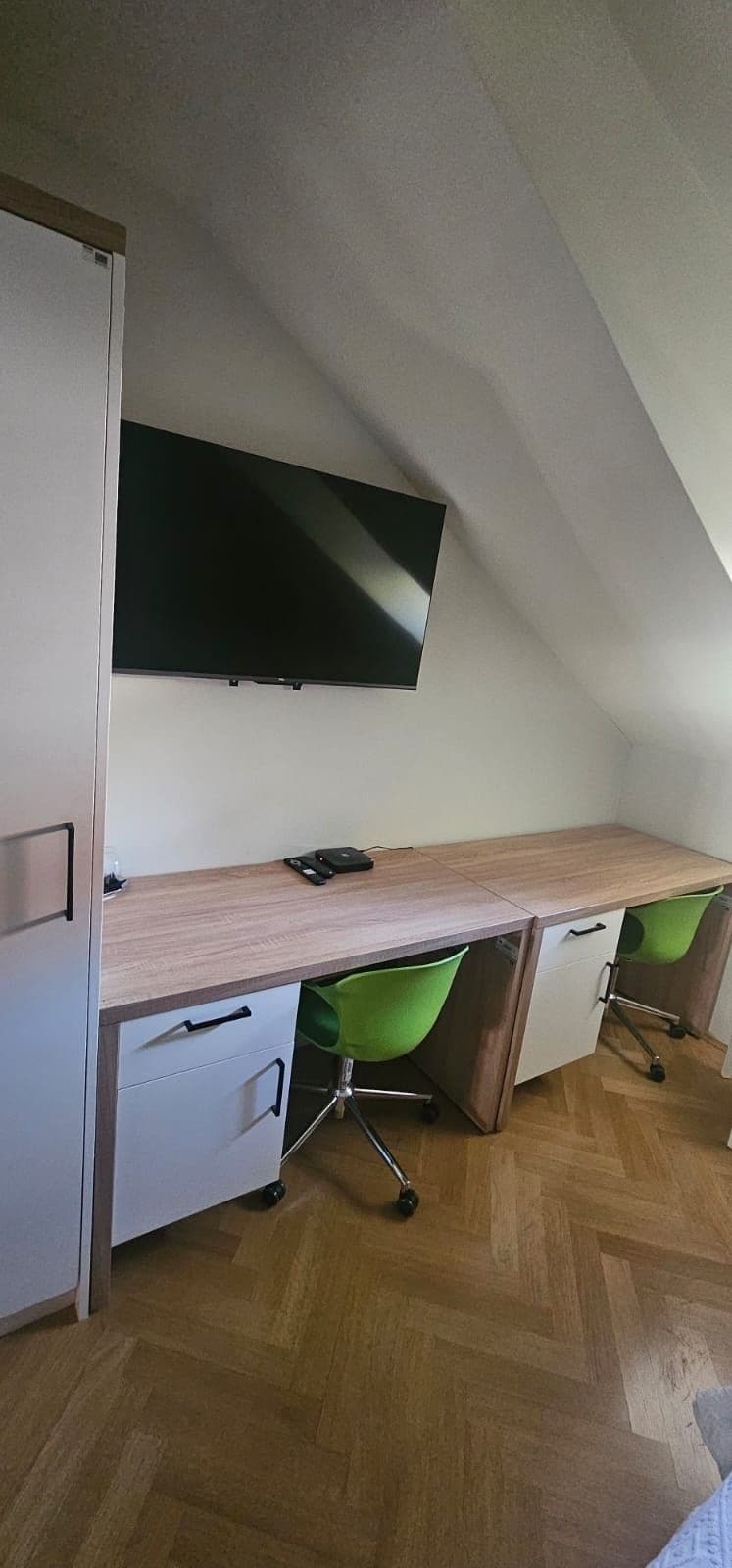 A room with a desk, a flat-screen TV mounted on the wall, and a green chair.