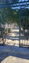 Uma entrada com portão e um caminho que leva a um edifício com fachada branca e janelas em arco.