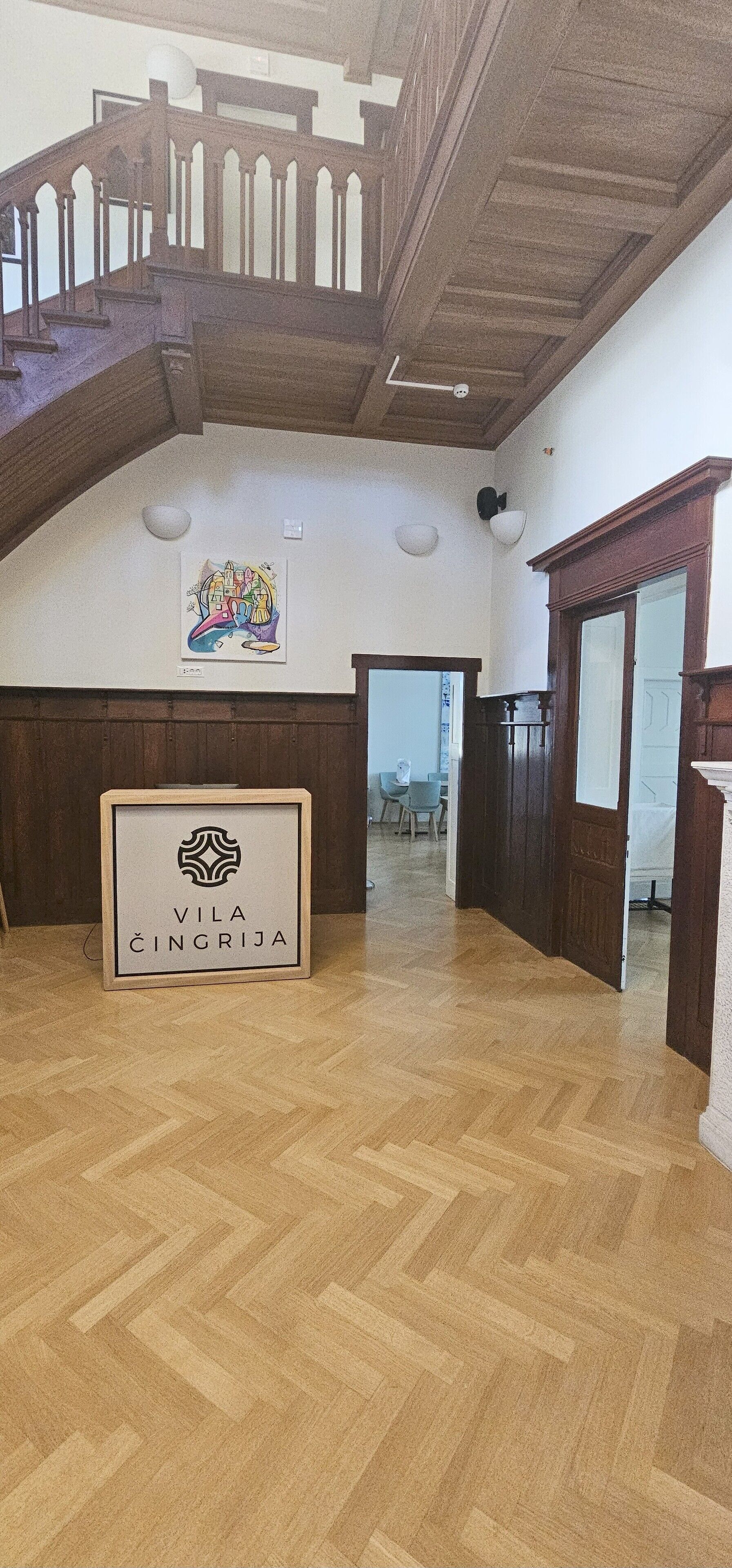 A spacious hall with a wooden staircase, a framed sign reading "VILA CINGRIZA", and a herringbone-patterned floor.