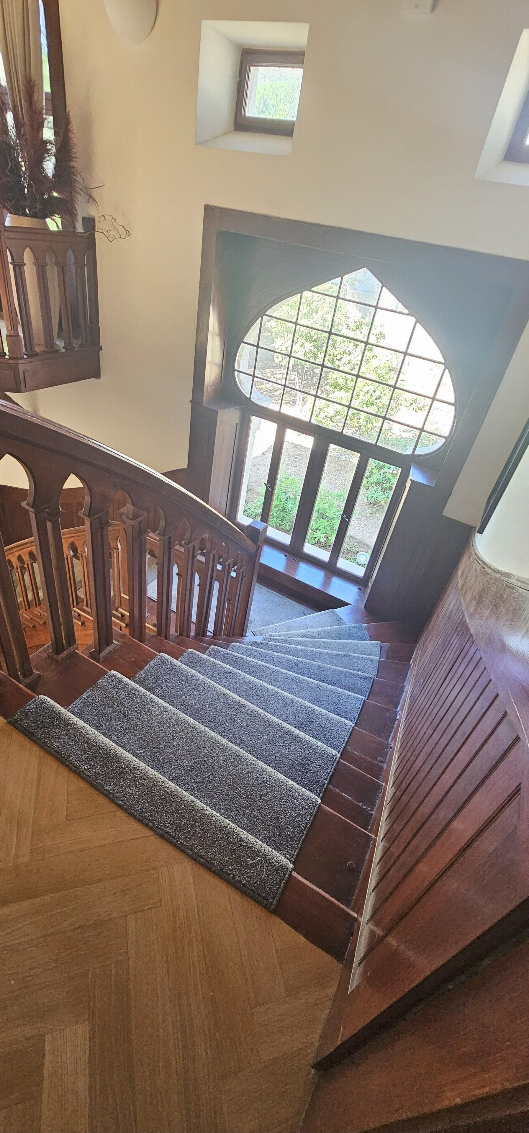 A wooden staircase with a carpeted landing and a view of the outdoors through a large window.