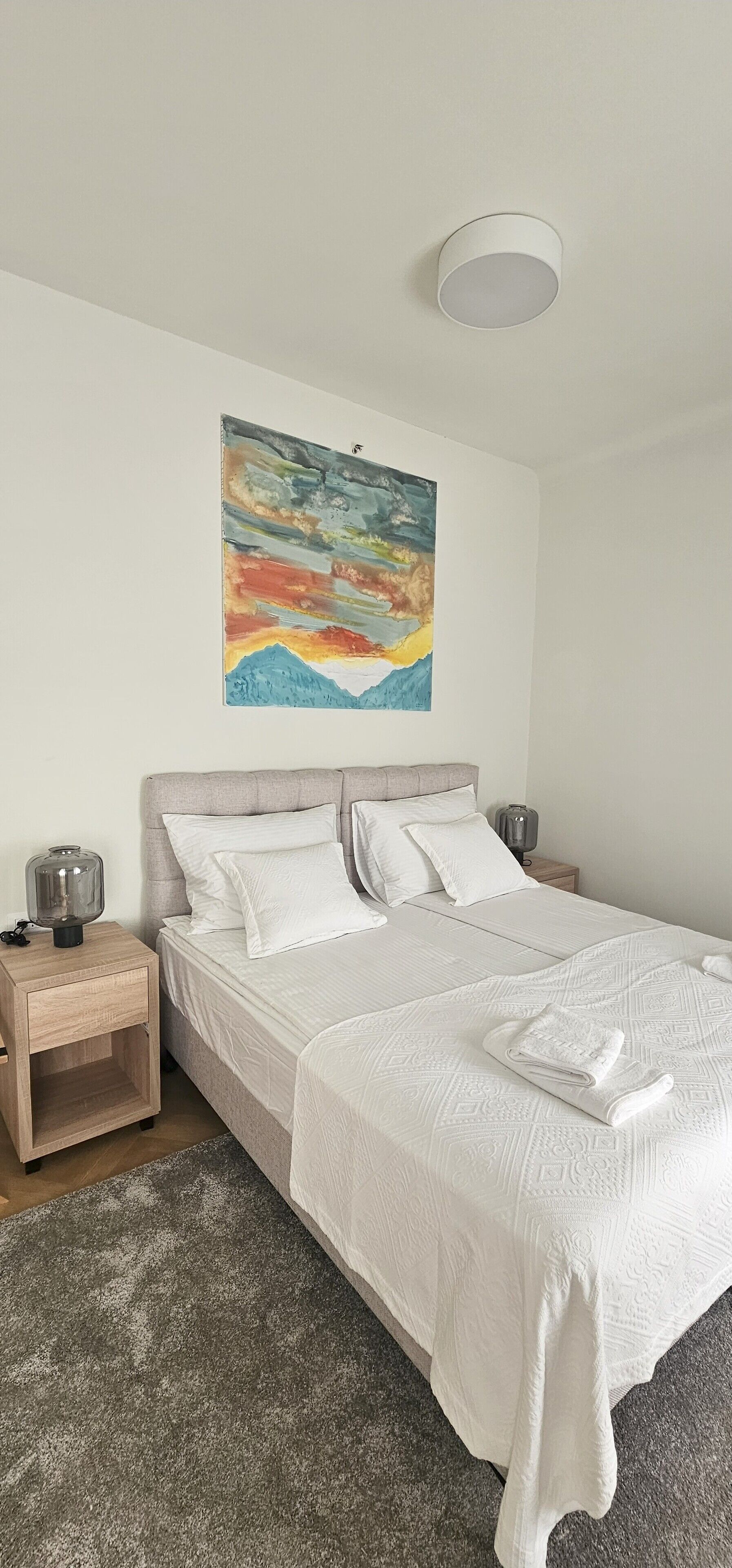 Un dormitorio con cama, mesitas de noche, un cuadro y una lámpara en el techo.