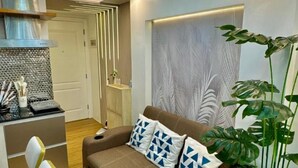 Una sala de estar moderna con un sofá marrón, cojines estampados, una araña, una zona de comedor con sillas y una planta grande en maceta.