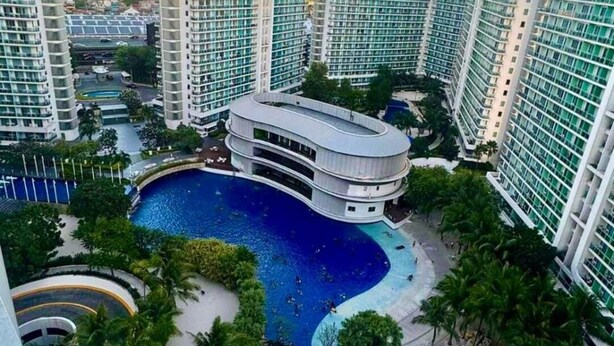 Un hotel moderno de gran altura con varias piscinas, un edificio central y abundante vegetación.
