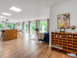 Un vaste espace de vie doté d’un plancher en bois, d’un canapé bleu, d’un téléviseur et d’un coin repas avec une table et des chaises en bois.