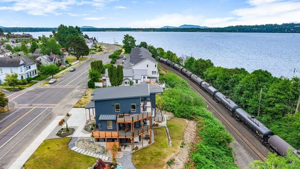 A modern two-story house with a balcony, a driveway, and a view of a lake and train tracks.