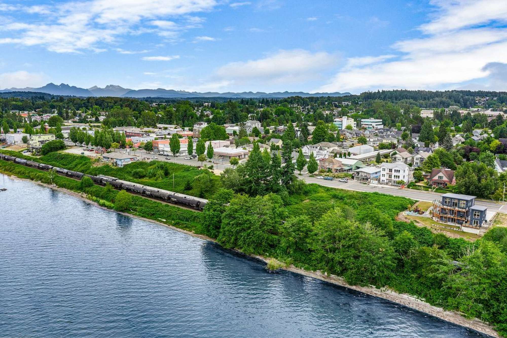 A riverside town with a train passing by, surrounded by greenery and residential buildings.