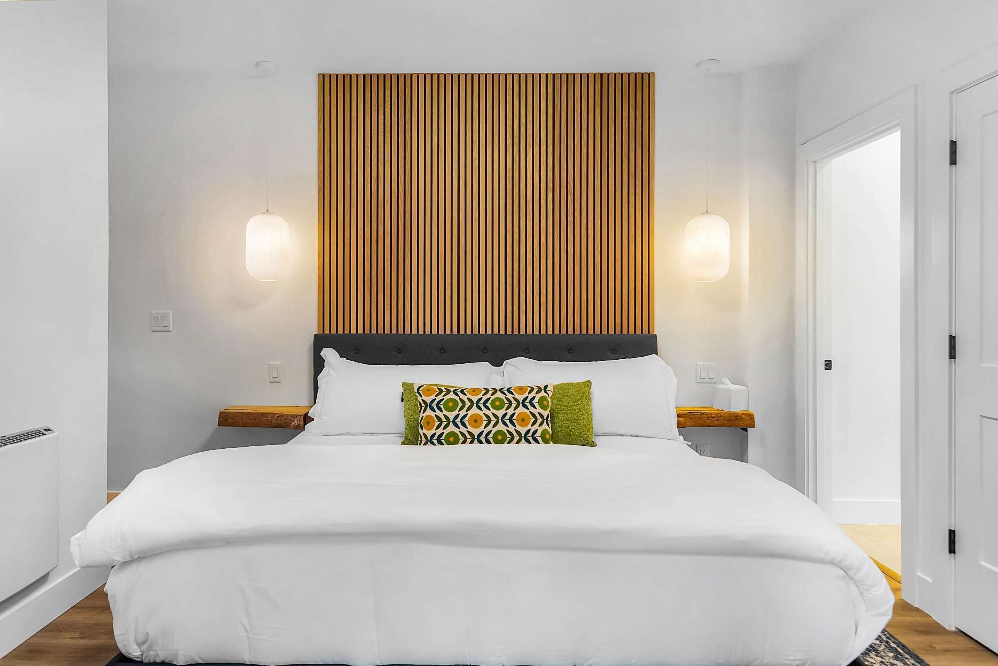 A modern hotel room with a large bed, wooden headboard, two bedside tables, and a nightstand.