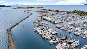 A marina with numerous boats docked, a large building, and a rocky breakwater.