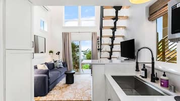 A modern kitchen with a built-in sink, a dining area with a sofa, and a large window providing natural light.