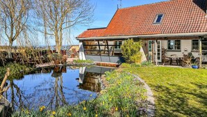 Ein Haus mit rotem Ziegeldach, einem Teich und einem Garten mit verschiedenen Pflanzen.