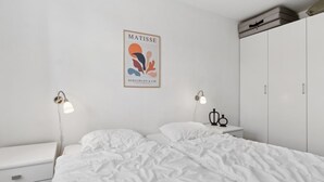 A minimalist bedroom with a large bed, two bedside tables with lamps, a wardrobe, and a framed artwork on the wall.