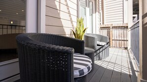 A balcony with wicker furniture, a potted plant, and a view of a building through the window. - Spacious 4-bedroom house Central Height Houston / w back yard & terrace (Houston)