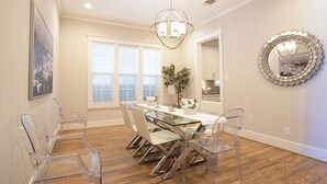 A dining area with a glass table and chairs, a chandelier, a large mirror, and a cityscape painting. - Spacious 4-bedroom house Central Height Houston / w back yard & terrace (Houston)