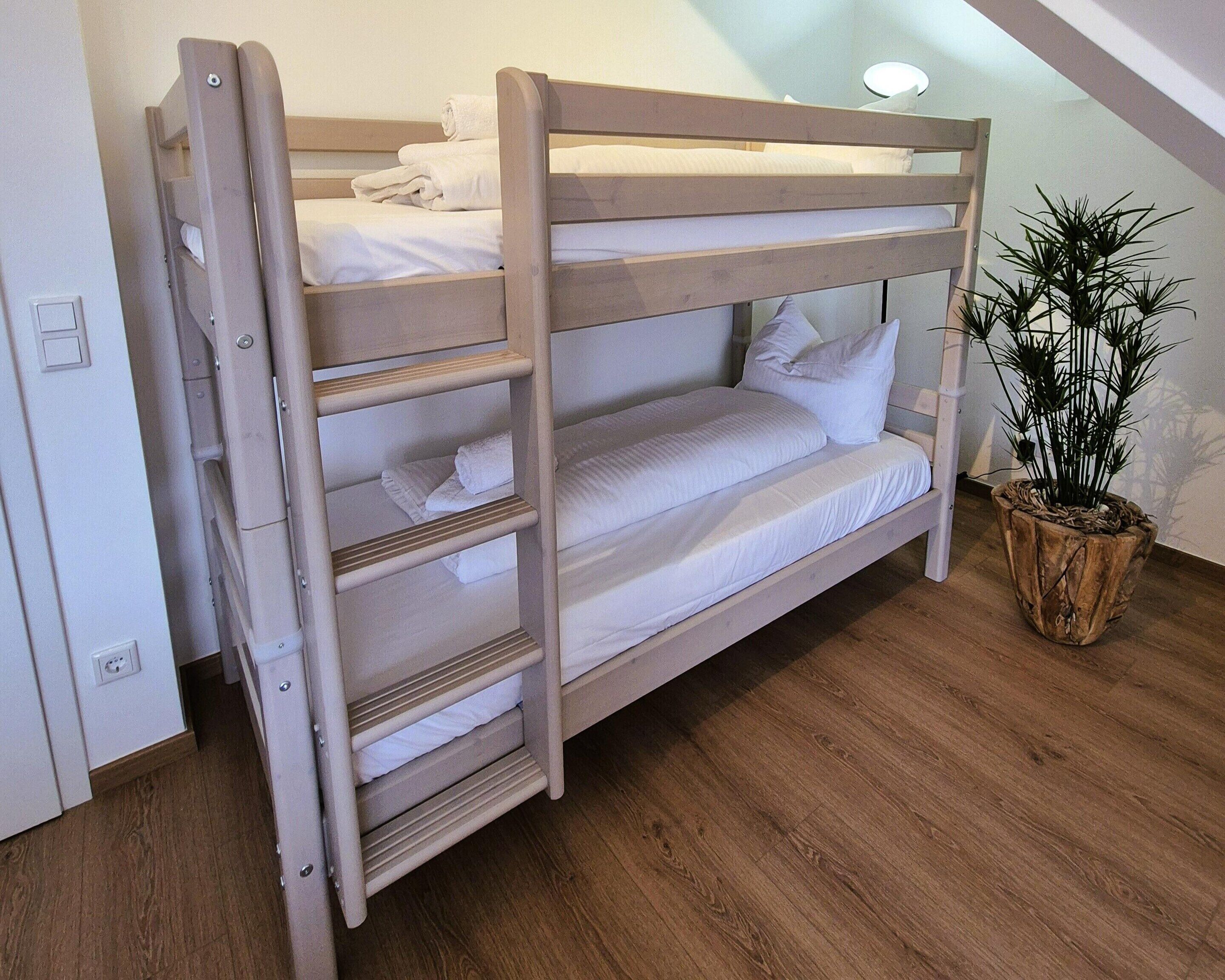 A bunk bed with white bedding, a wooden floor, and a potted plant.
