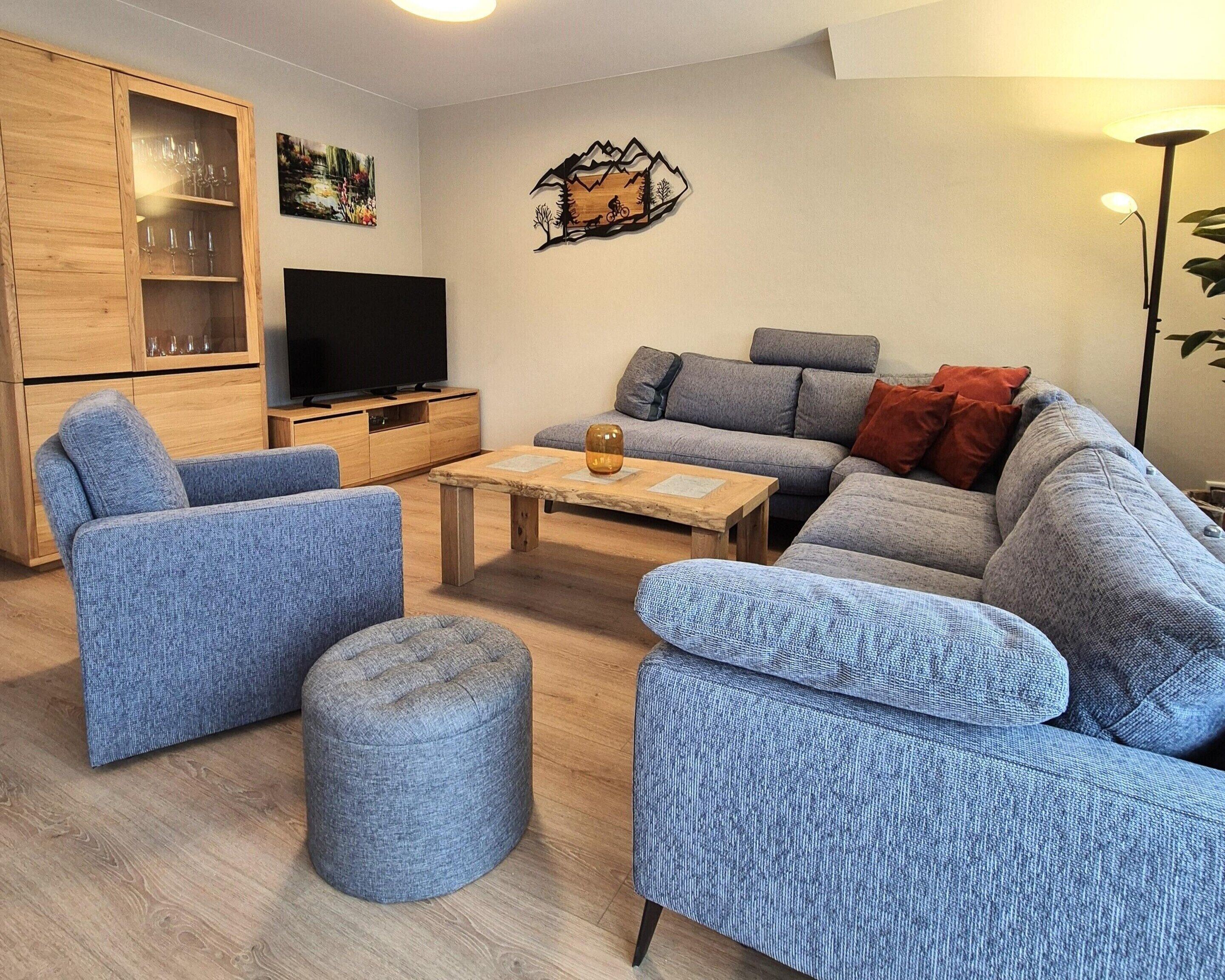 Ein modernes Wohnzimmer mit grauem Sofagarnitur, einer Holzvitrine mit Glastüren, einem Flachbildfernseher und einem Couchtisch.