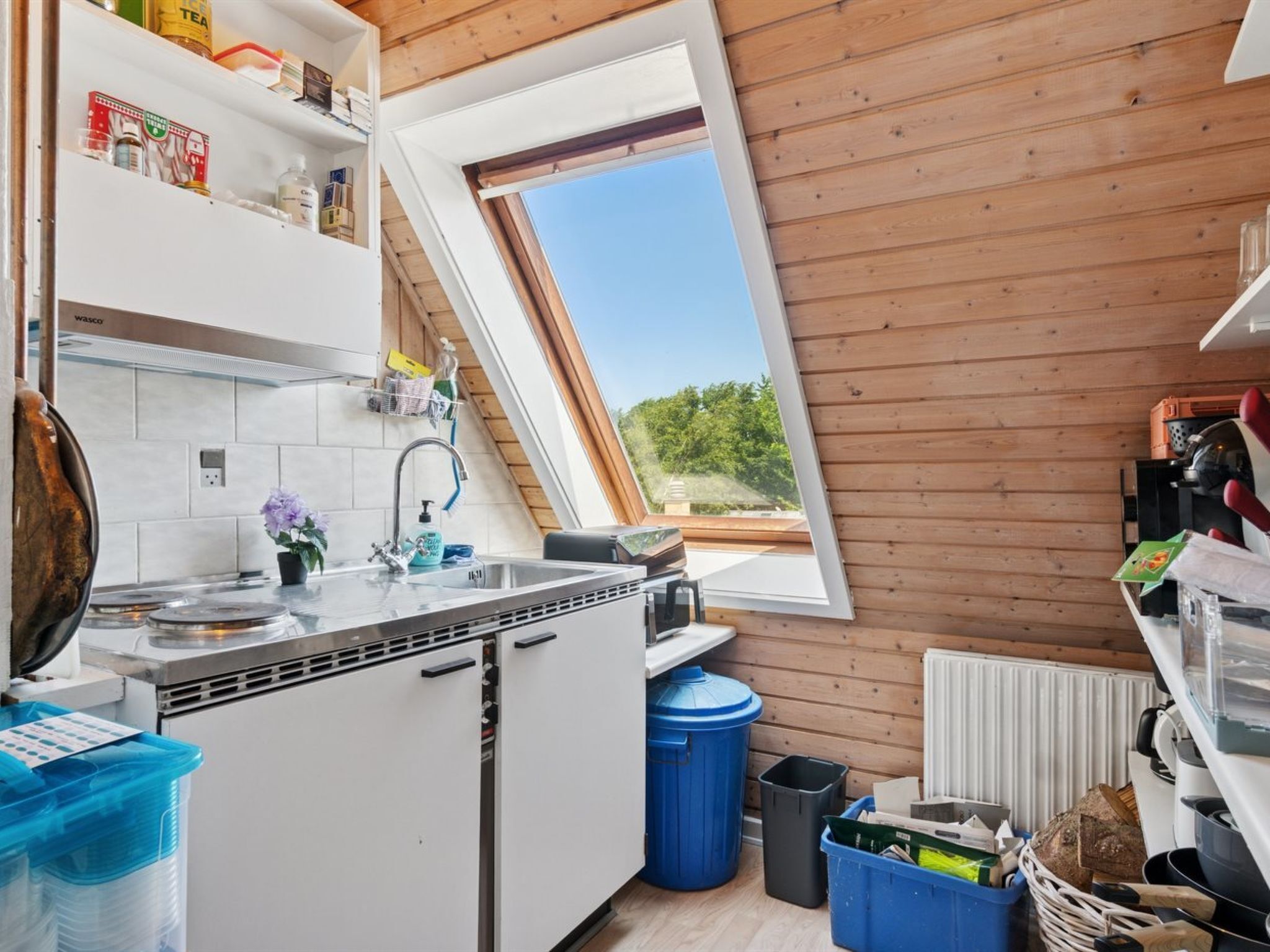 Eine kleine Küche mit Dachfenster, weißen Schränken und Blick ins Grüne.