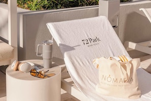 Een ligbed met een handdoek, een waterfles en een tas met de tekst 'NOMADA' op een terras.