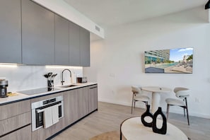 A modern kitchen with built-in appliances, a dining area with a round table and chairs, and a large window with a view of a building.