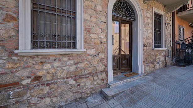 A stone building with arched windows and a door, a tiled ground, and a staircase leading to an upper level.