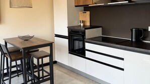Una cocina moderna con comedor, con una paleta de colores blanco y negro, horno empotrado y cafetera.