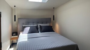 Un dormitorio con tragaluz, una cama con ropa de cama a rayas, una mesita de noche y una lámpara.